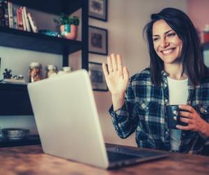 mosolygós nő kávéval a laptop előtt integet